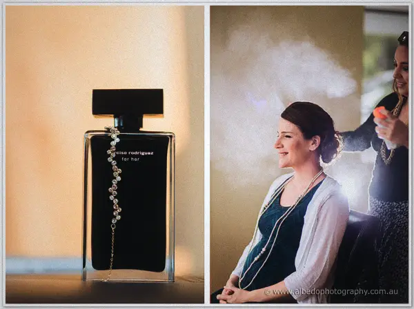Black perfume bottle strung with pearls sits beside the bride having her updo misted and styled