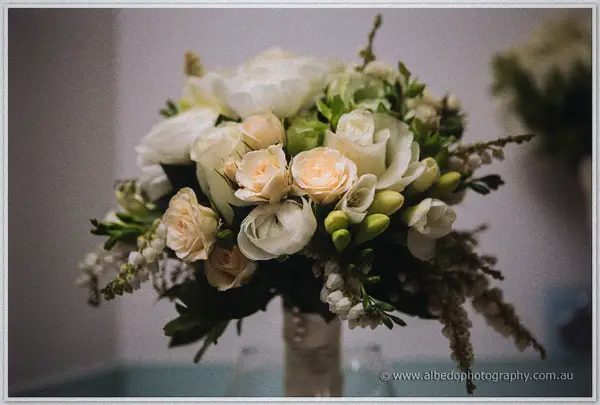 Bridal bouquet of cream roses, ranunculus and berries bursts from a pearl-studded ribbon wrap