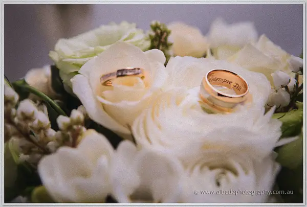 Two wedding rings nestled into white and cream roses in the bridal bouquet, soft light on the petals.