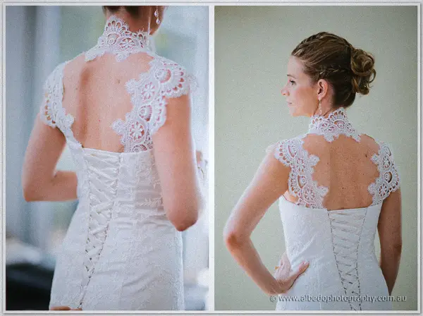 Back view of the bride's corset-laced gown and sheer guipure lace capelet across bare shoulders.
