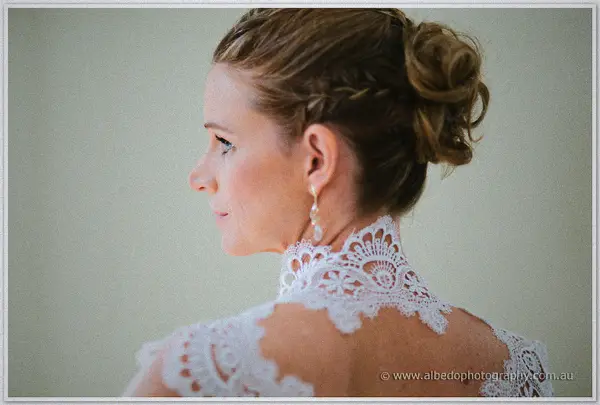 Profile of the bride showing a braided chignon and the delicate lace collar of her wedding dress.