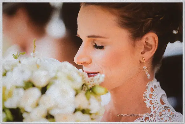 Close profile of the bride behind a creamy white rose bouquet, drop earring and lace shoulder in view.