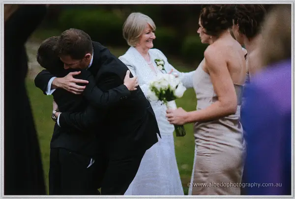 Groom sharing a hug with a guest on the lawn as smiling family look on at Silkwood Winery, Pemberton.