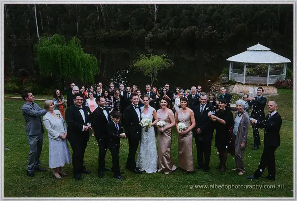 Wedding party gathered on the lawn as guests toss petals, forest rising behind the Pemberton winery.
