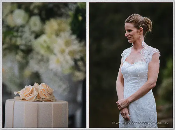 Cream wedding cake crowned with peach roses beside the smiling bride in her lace gown.