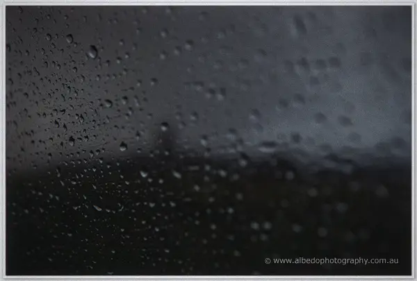 Raindrops streaking a dark window pane against a stormy grey Pemberton sky.