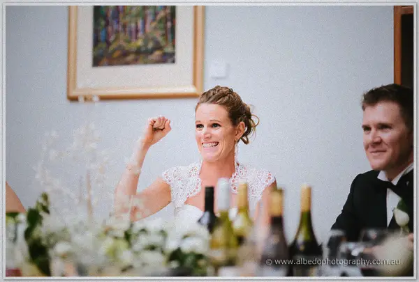 Bride raising a triumphant fist and laughing during the wedding speeches.