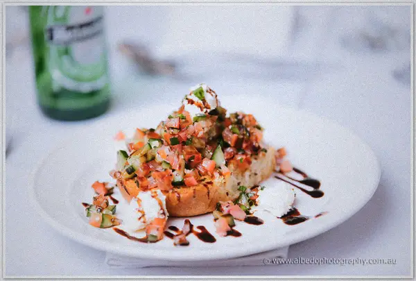 Bruschetta piled with tomato salsa and a balsamic drizzle on a white plate.