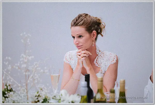 Bride clasping her hands thoughtfully beneath her chin while listening to speeches.