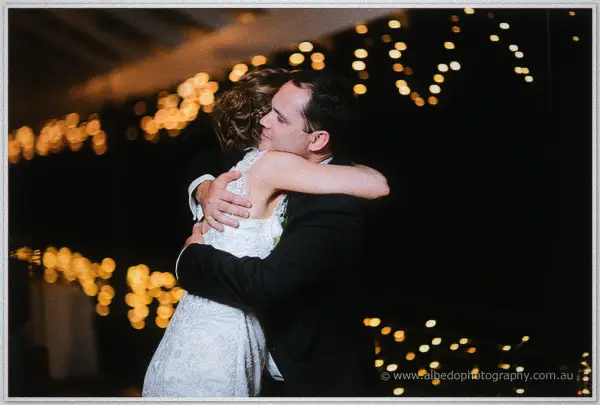 Bride and groom hugging tight amid golden bokeh of festoon lights at Silkwood Winery.