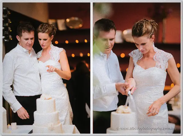 Groom guiding the bride's hand to cut their three-tier cake in candlelight at Silkwood.