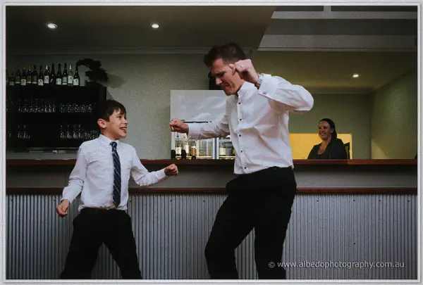 Groom and young page boy fist-bumping and dancing beside the bar at the reception.