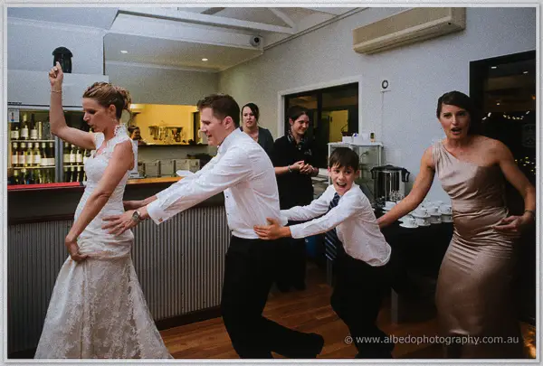 Bride, groom, page boy and bridesmaid forming a conga line through the venue at night.