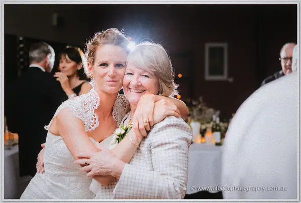 Bride embracing her proud older mother among the candlelit reception guests.