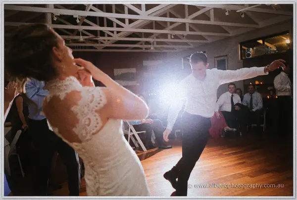 Groom spinning dramatically across the dance floor in a burst of warm backlight.