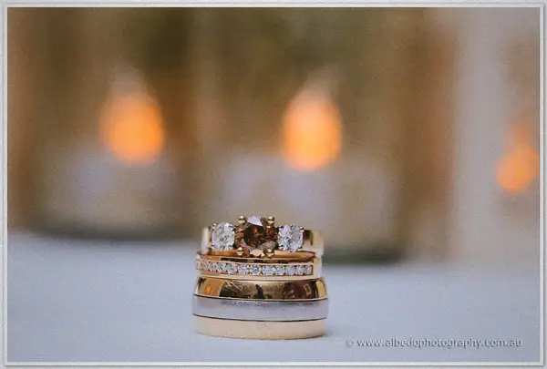Stacked gold and white-gold rings with a champagne diamond against warm candle bokeh.
