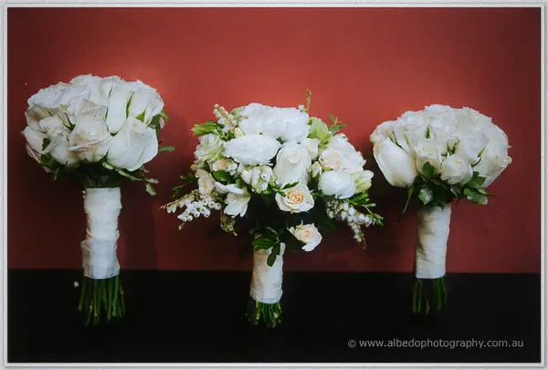 Three white rose bouquets lined up against a deep red wall at the winery.