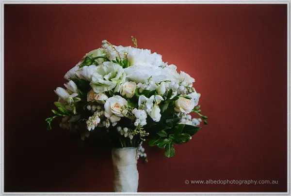 Bride's white and blush bouquet with trailing greenery against a deep red wall.