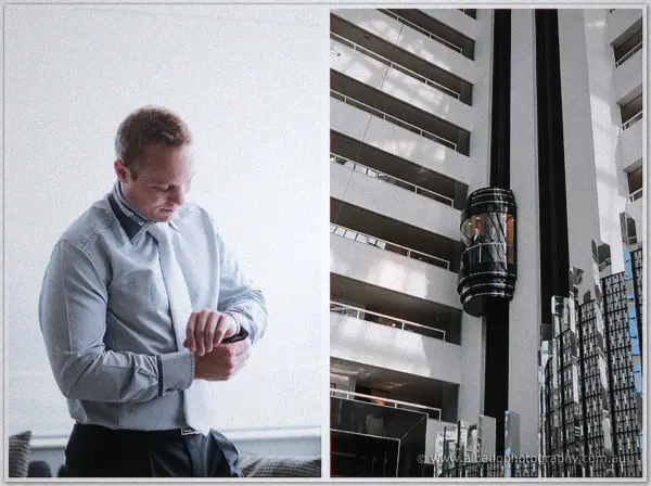 Nathan fastens his watch in soft window light beside the hotel's black cylindrical elevator shaft