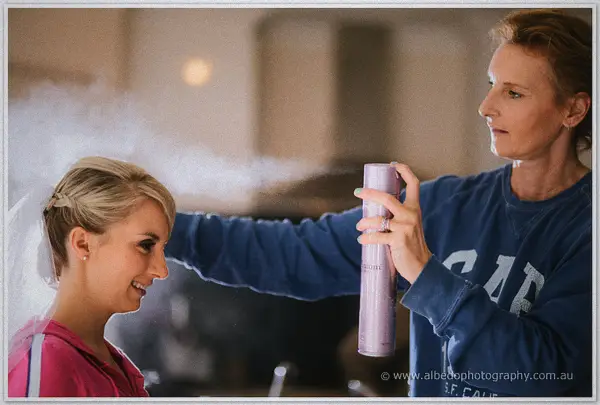 A stylist blasts hairspray over Sarah's veiled updo, mist drifting through the warm morning light