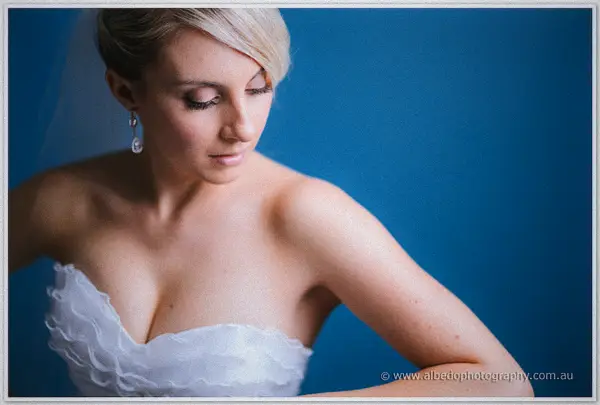 Sarah gazes down through lidded eyes, her earrings catching light above the ruffled sweetheart neckline
