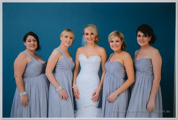 Sarah stands mid-laugh with her four bridesmaids in matching grey gowns against the deep blue wall