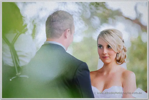 Sarah looks up at Nathan through leafy bokeh, her chignon pinned with a small clip