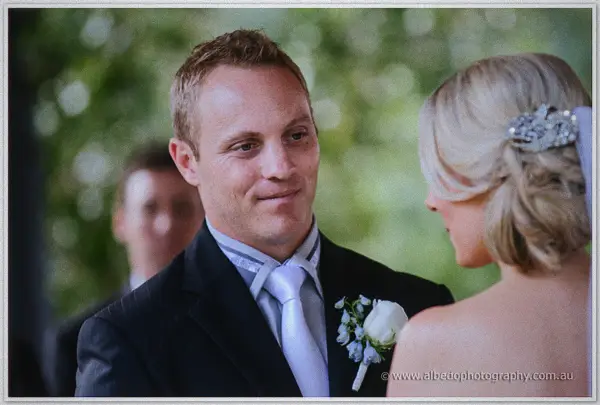 Nathan's eyes glisten as he faces Sarah, her crystal hairpiece sparkling against blurred gum trees