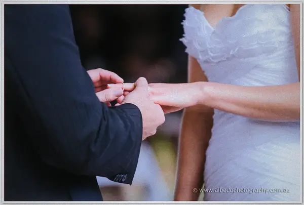 Nathan slides a ring onto Sarah's finger, her ruffled gown catching light against his dark suit