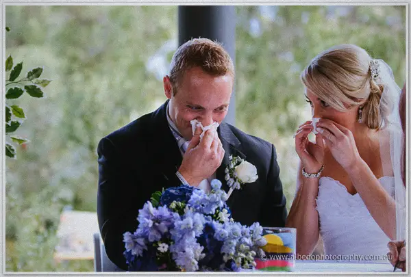 Sarah and Nathan dab tears with tissues during their vows, blue hydrangea bouquet before them