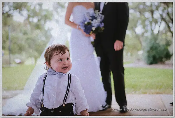 A cheeky page boy in suspenders grins ahead of Sarah and Nathan on a Kings Park garden path