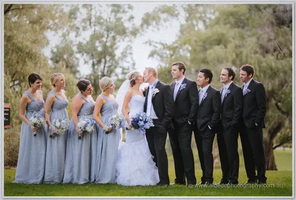Sarah and Nathan kiss between grey-gowned bridesmaids and black-suited groomsmen in Kings Park