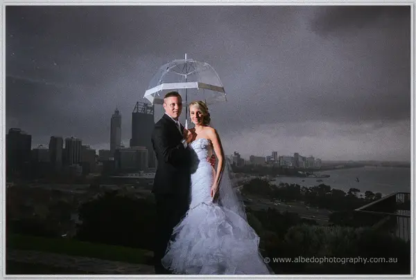 Nathan shelters Sarah beneath a clear umbrella as storm clouds gather over the Perth skyline
