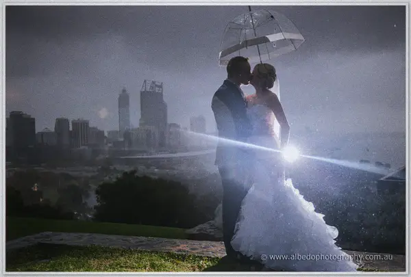 A kiss beneath an umbrella in the rain, city towers of Perth blurred behind the glowing newlyweds