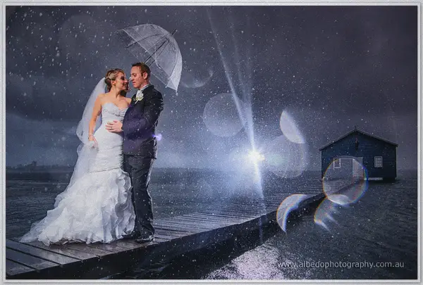 Rain streaks past Sarah and Nathan on a jetty by the Crawley Edge Boatshed at dusk