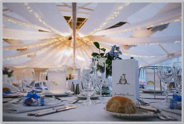 A Joondalup Resort table set with glassware, blue hydrangeas and fairy lights strung overhead