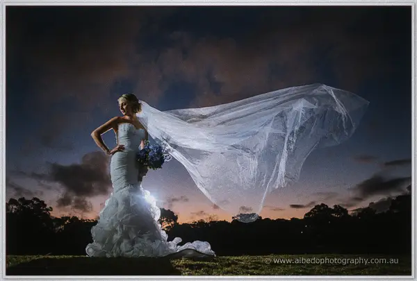 Backlit at dusk, Sarah rests a hand on her hip as her veil billows across the darkening sky