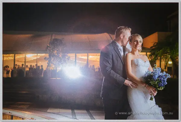 Nathan nuzzles Sarah's temple by the pool as fairy-lit reception marquees glow behind them