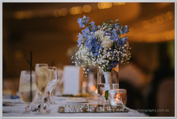 A blue and white bridesmaid bouquet resting in a glass vase amid candlelit reception tables