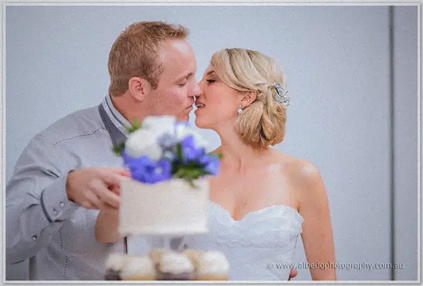 A kiss over the cake, Nathan still holding the knife as the blue-flowered tier sits between them