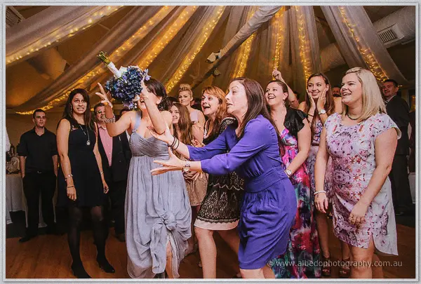 A bridesmaid in grey catches the blue bouquet ahead of a lunging guest in purple