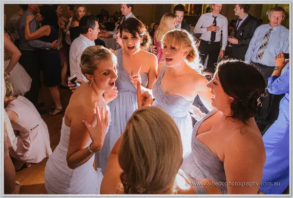 Sarah and her bridesmaids in lavender sing along in a circle, one pointing to the beat