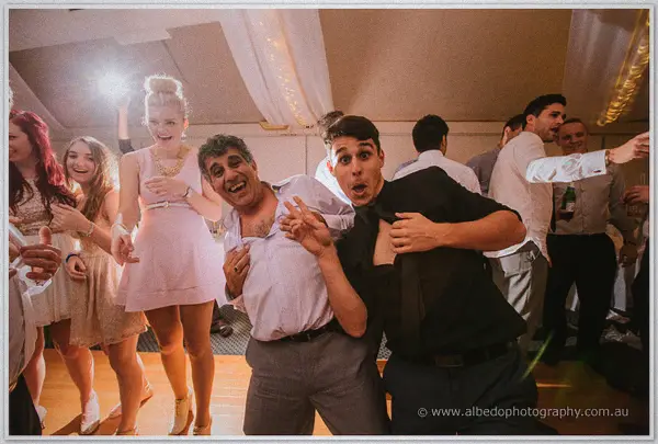 Two guests mug for the camera with wild faces and loosed ties as a pink-dressed friend dances