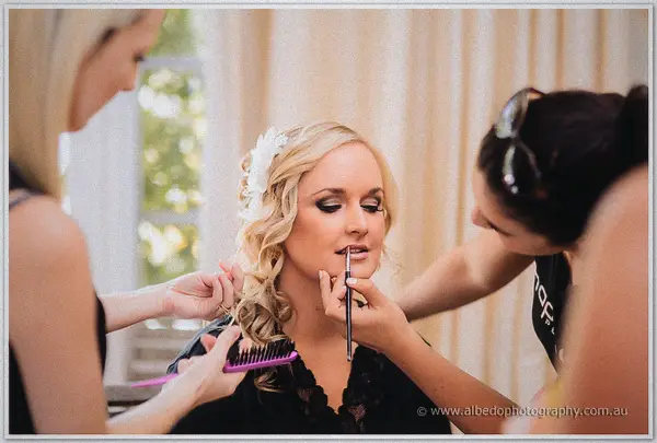 Ashley sits with curled hair and a flower clip as stylists apply her makeup and comb her waves