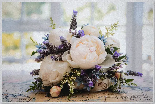Peonies, lavender and soft blue blooms cluster into a lush bouquet resting on a vintage map