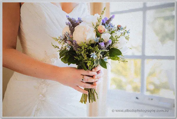 Ashley cradles her peony and lavender bouquet against her gown beside a bright country window