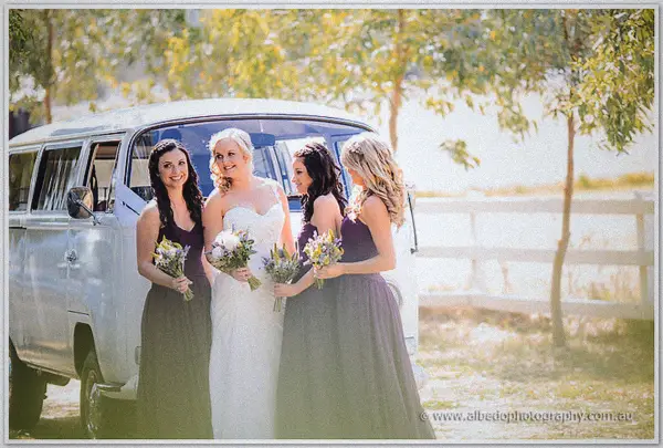 Ashley and her bridesmaids beam beside a white Kombi van beneath sunlit trees by a ranch fence