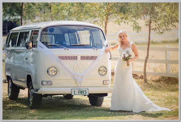 Ashley leans on a ribboned Kombi van's bonnet with her bouquet on the lawns of Carilley Estate