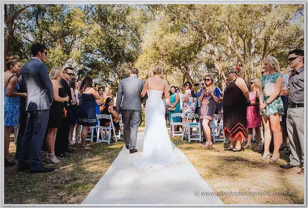 Bride walking down the aisle arm in arm with her father among seated garden guests