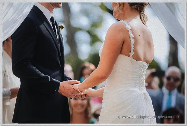 Couple holding hands beneath sheer ceremony fabric in dappled sunlight